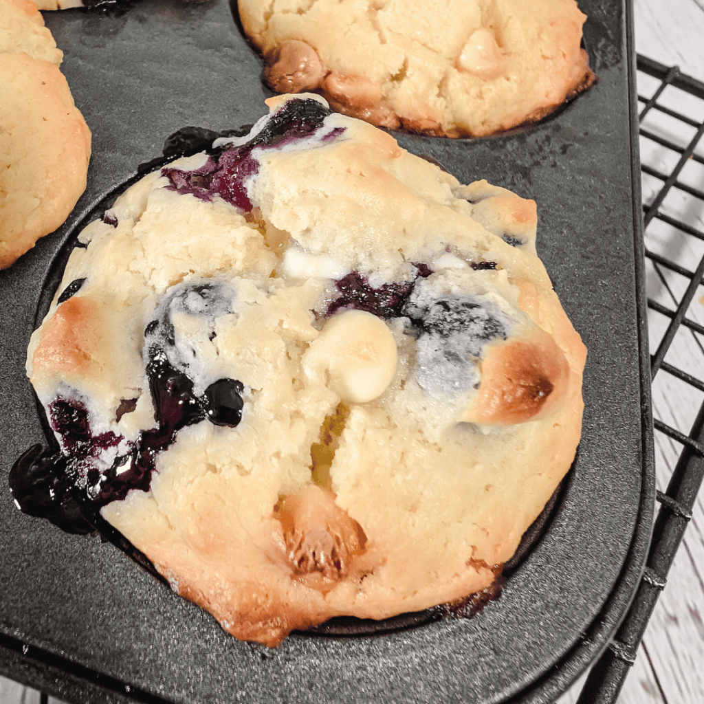 Freshly baked chocolate chip cookie with blueberries on a baking sheet.