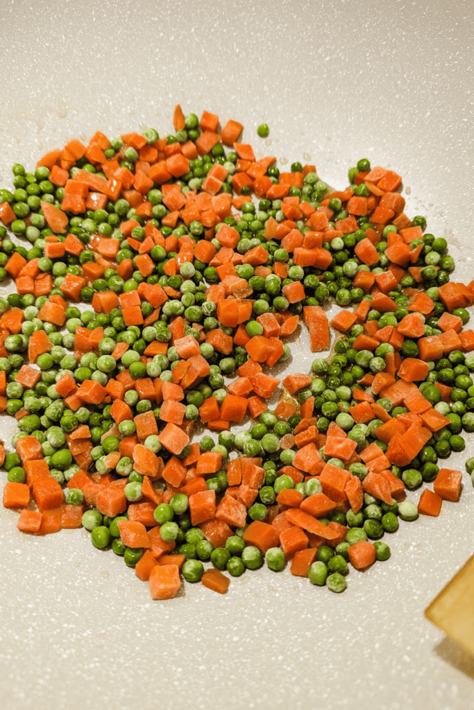 Stir-fried shrimp, rice, carrots, and peas in a non-stick pan for a quick weeknight dinner.