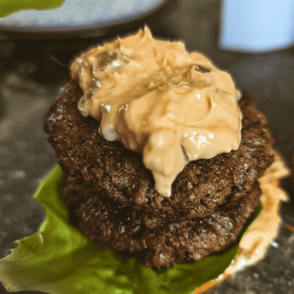 Juicy burger patty topped with creamy cheddar cheese sauce on lettuce.