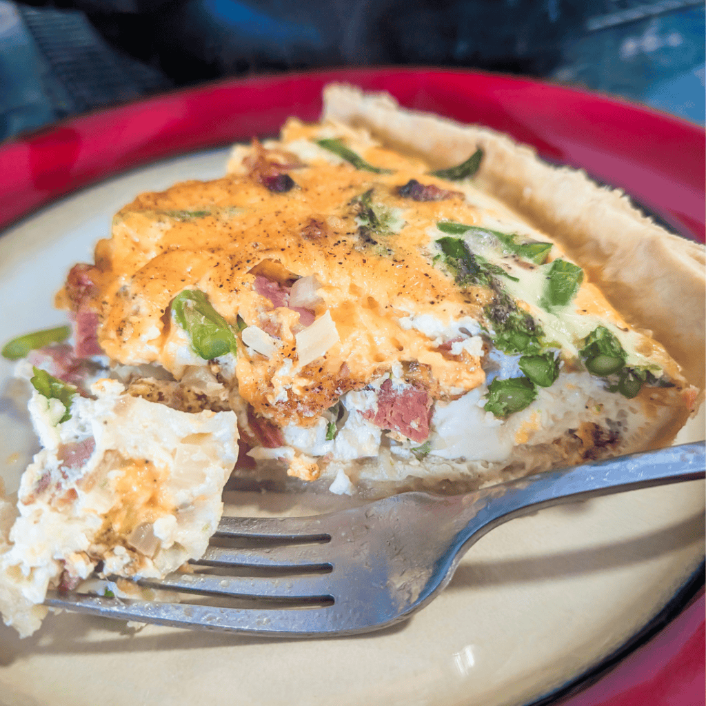 Delicious ham and asparagus quiche slice on a plate.