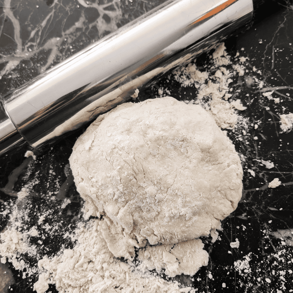 Freshly prepared pie dough for ham and asparagus quiche on a black marble surface.