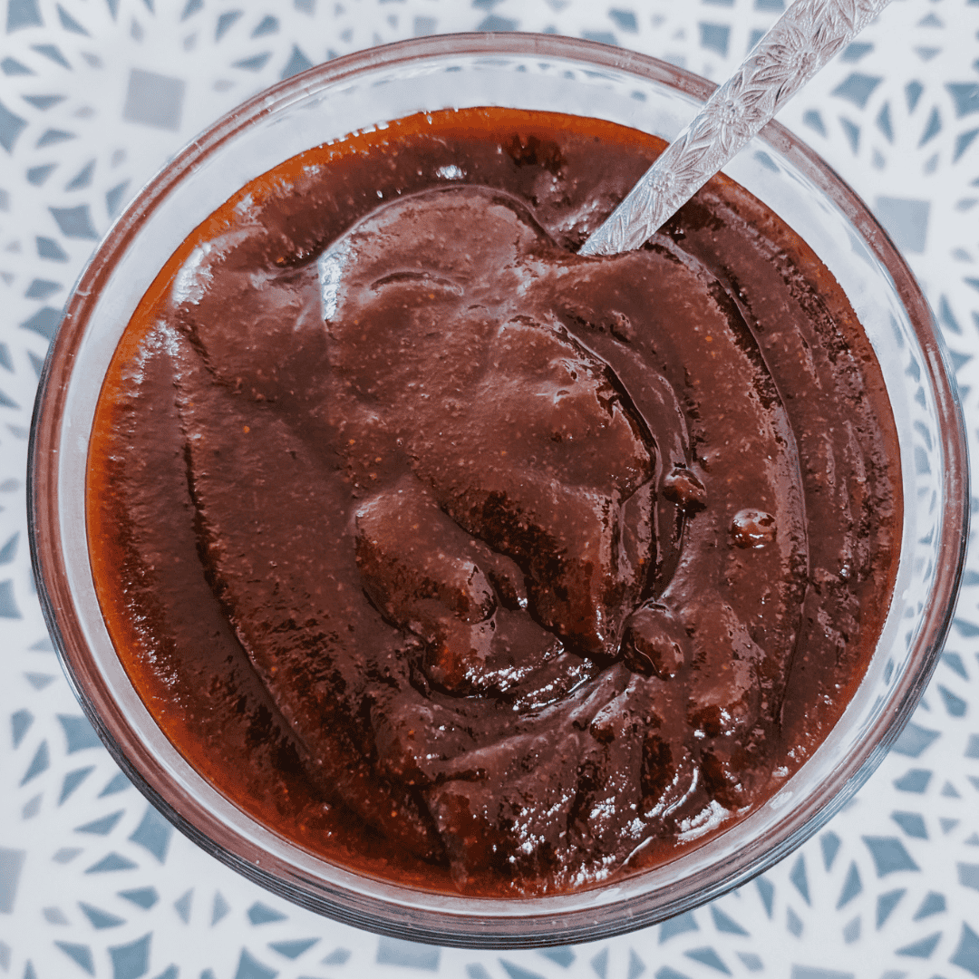 Close-up of homemade sweet smoky molasses BBQ sauce in a glass jar with a spoon.