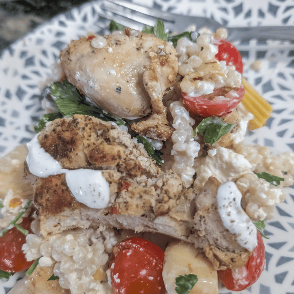Chicken couscous salad with cherry tomatoes and Greek yogurt dressing on a decorative plate.