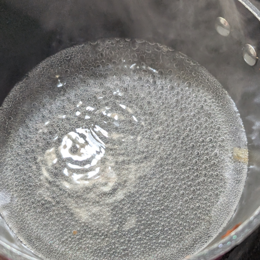 Water boiling in a pot with bubbles forming at a rolling boil.