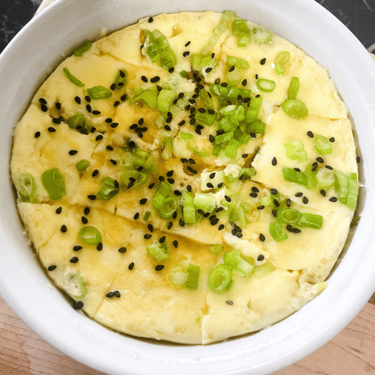 Egg dish topped with chopped green onions and black sesame seeds in a white bowl.