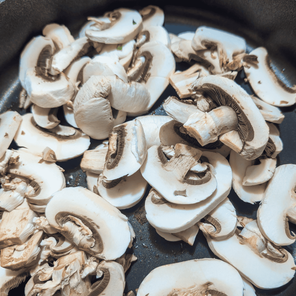 Sliced fresh mushrooms in a skillet for mushroom rice pilaf.
