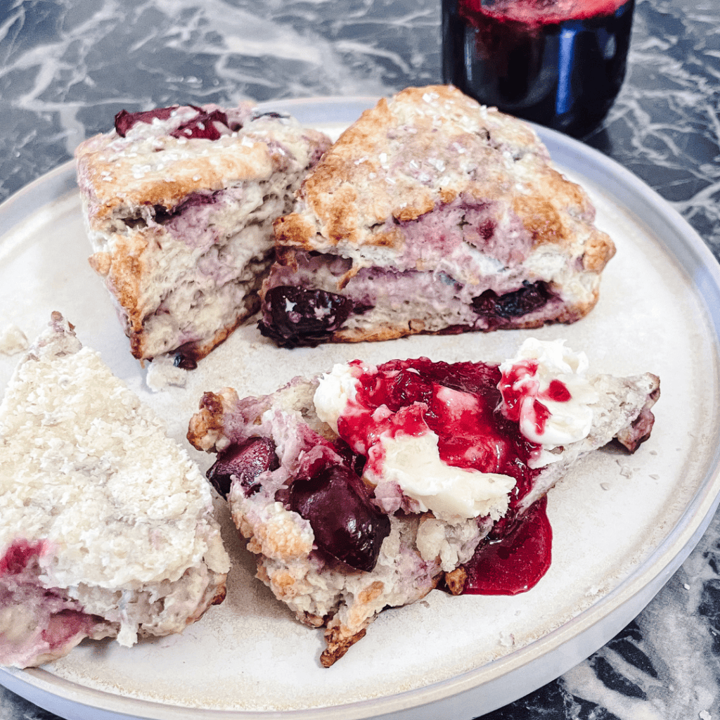 Fresh cherry scones with cherries and cream on a plate, perfect for breakfast or snack.