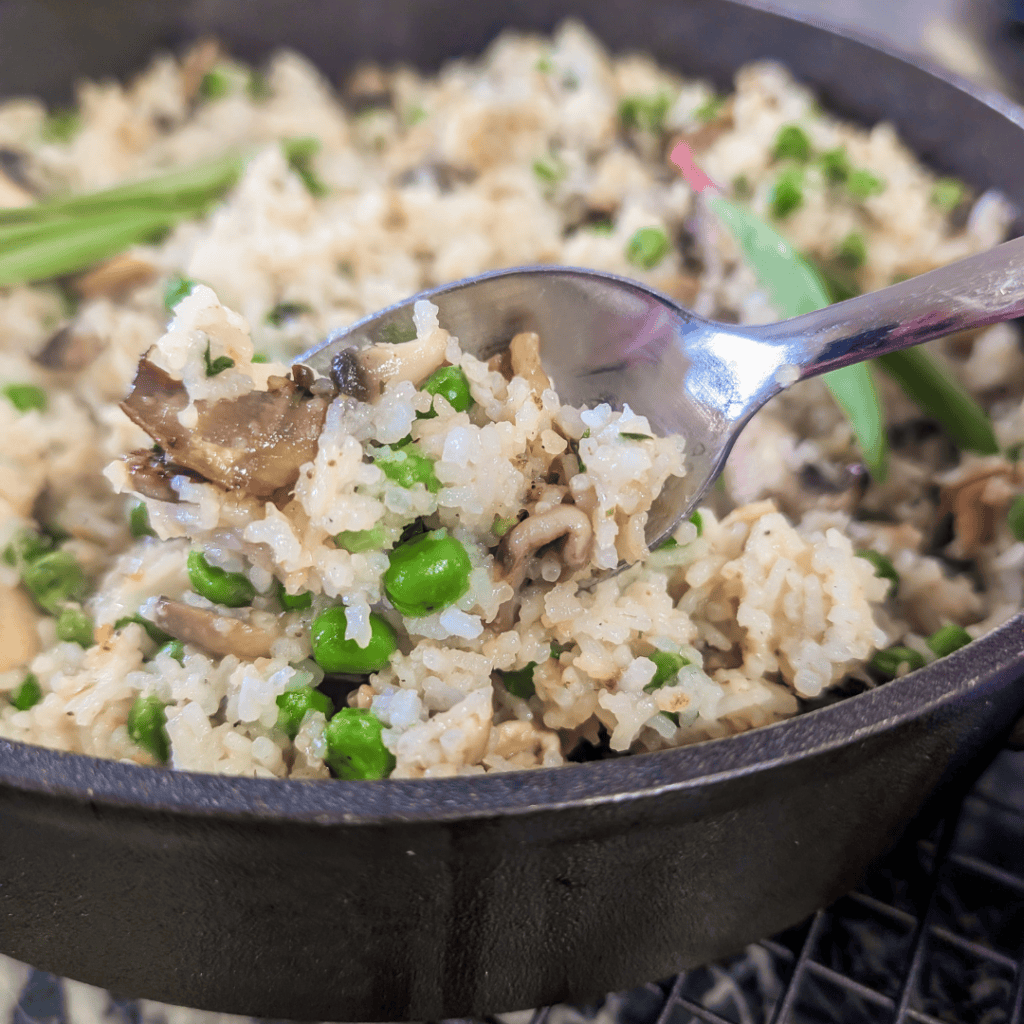 Close-up of mushroom rice pilaf with ramps and peas in a skillet.
