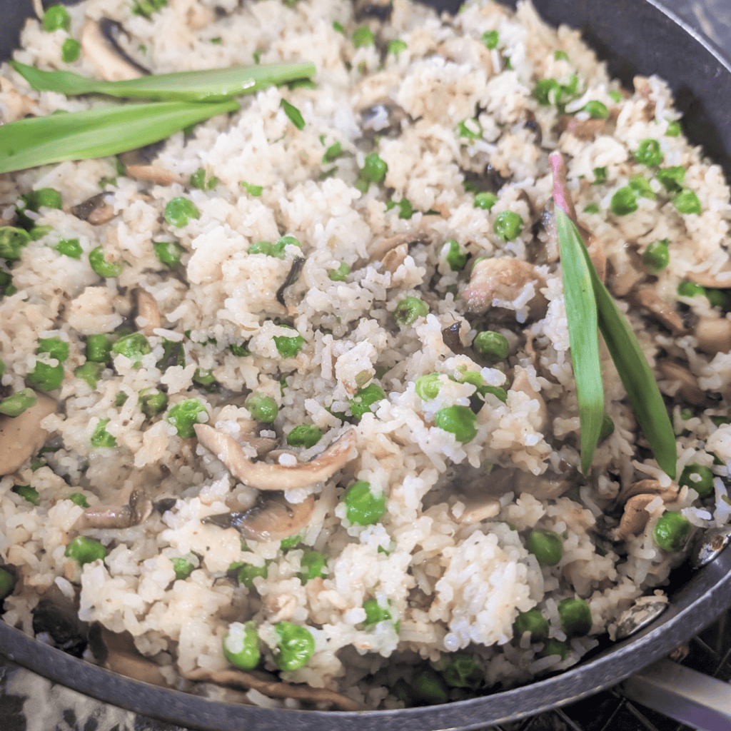 Mushroom rice pilaf with ramps and peas in a skillet, fresh herbs.