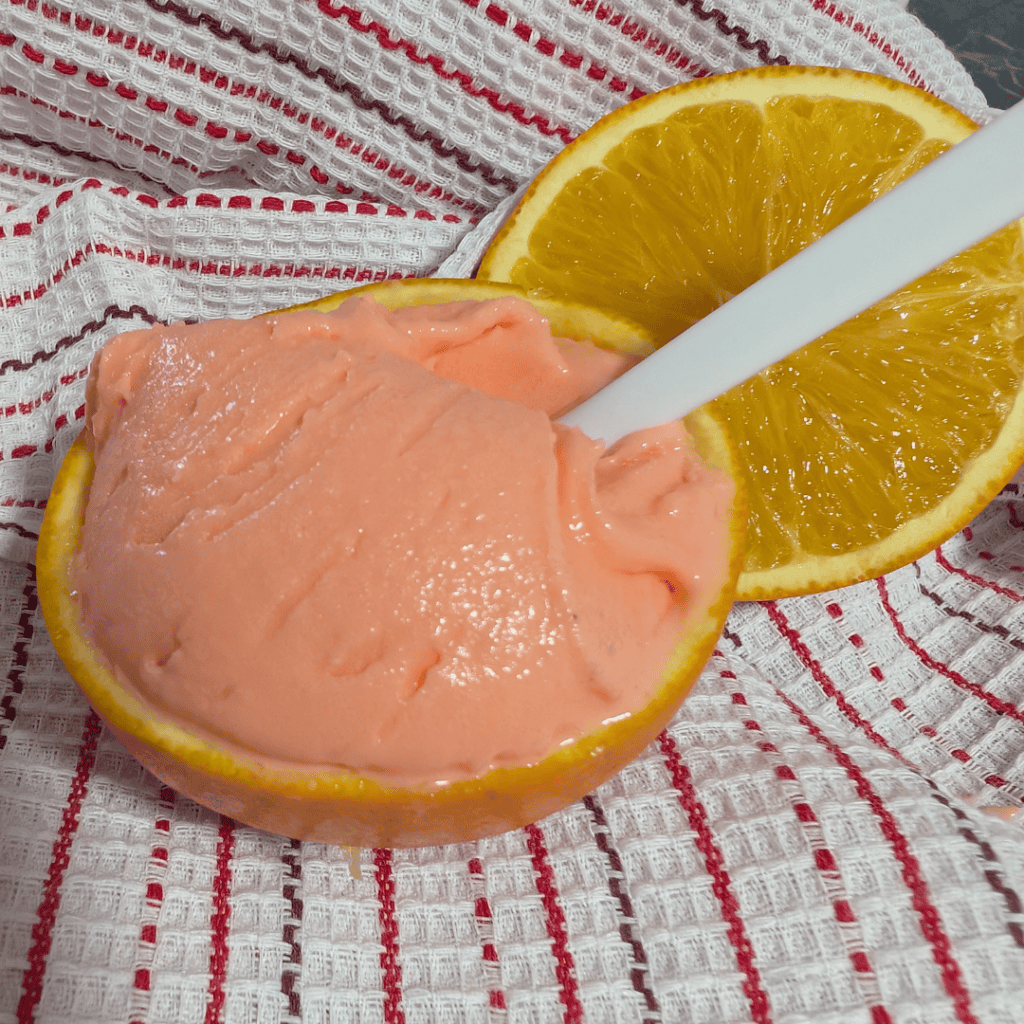 Creamy orange creamsicle ice cream served in a halved orange with a straw.