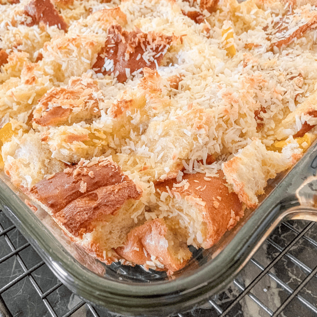 Delicious mango bread pudding topped with shredded coconut in a glass baking dish.