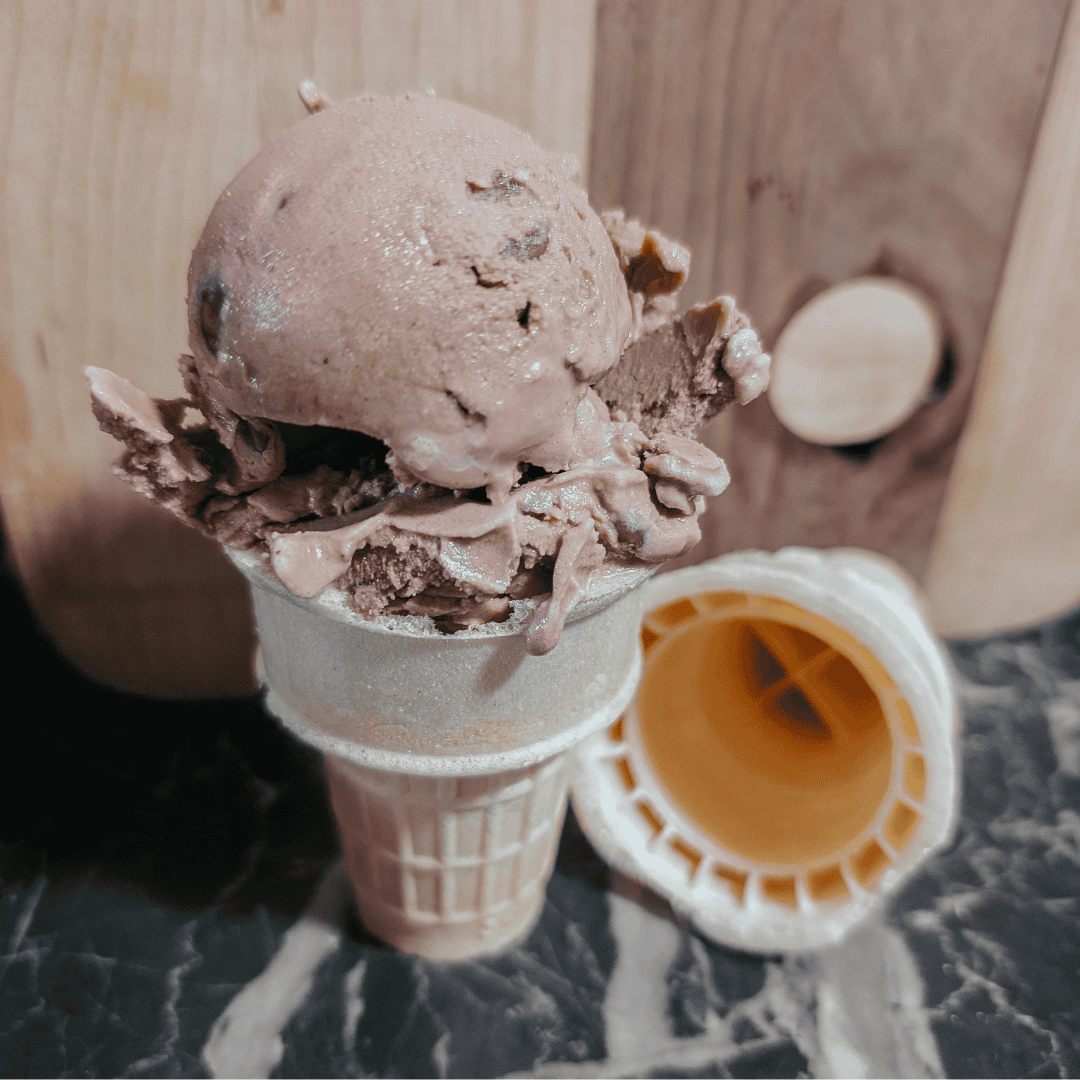 Delicious chocolate ice cream served in a waffle cone, topped with chocolate chunks and drizzled wit.