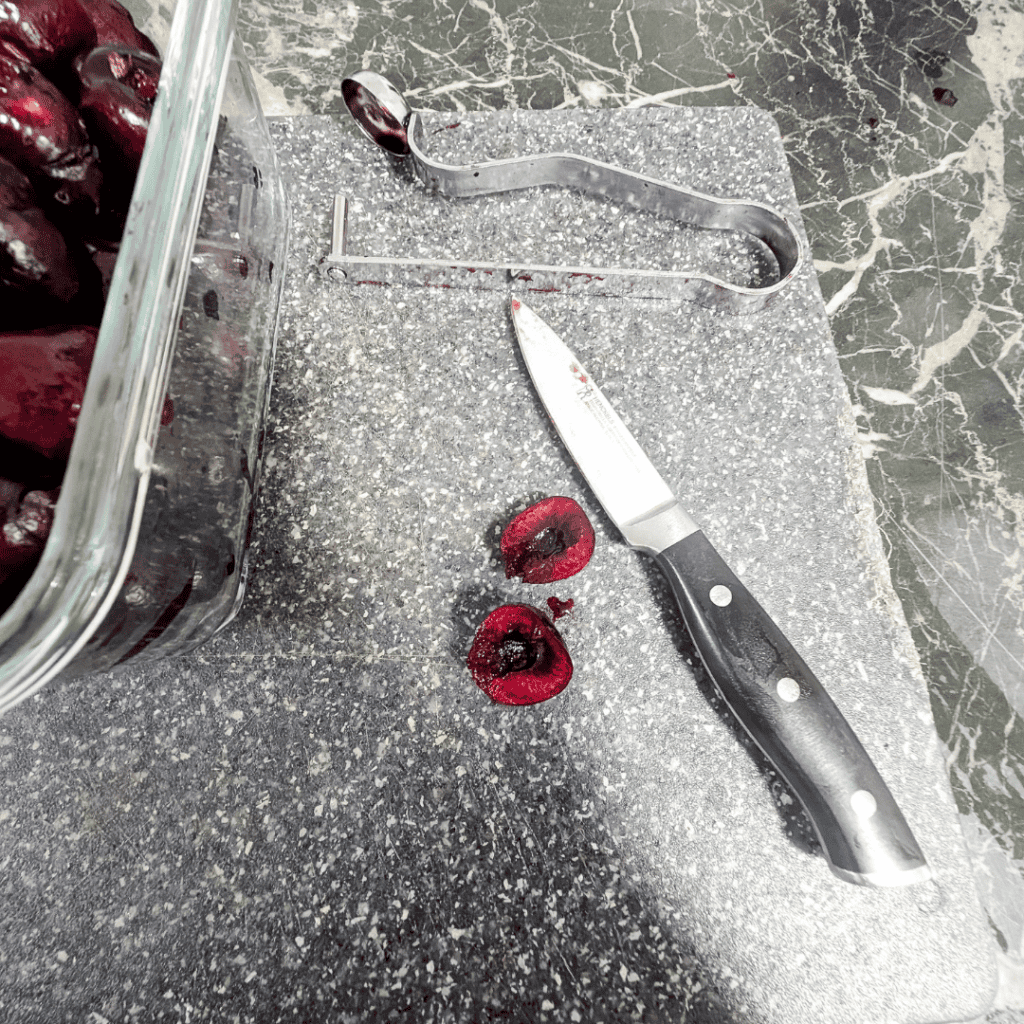 Cherry pits and a knife on a kitchen countertop for cherry preparation.