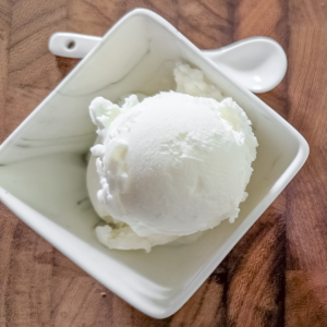 Creamy vanilla ice cream scoop in a white bowl on wooden surface.