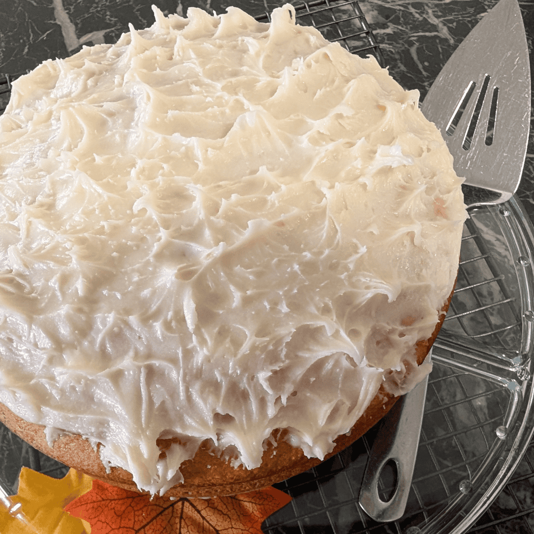 the frosted pumpkin cake on glass cake plate with cake lifter beside