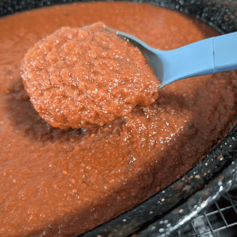 Close-up of homemade roasted tomato sauce in a pan with a blue spoon.