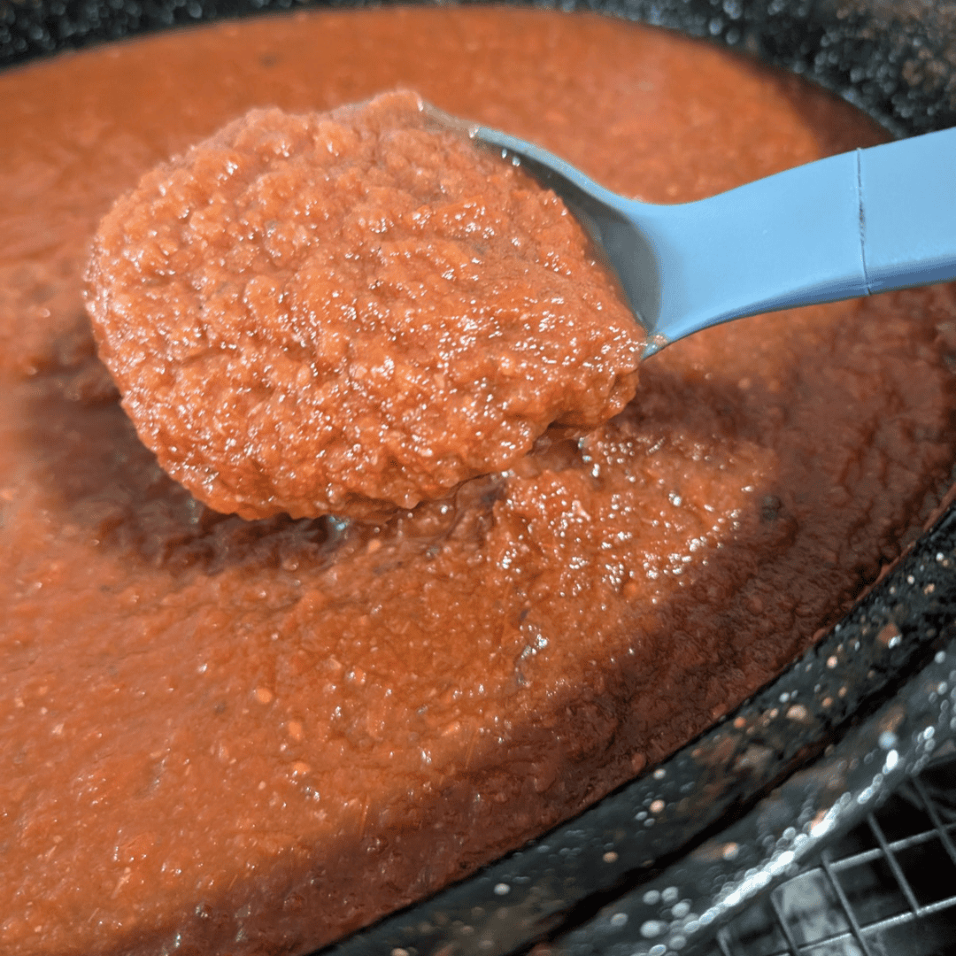 Close-up of homemade roasted tomato sauce in a pan with a blue spoon.
