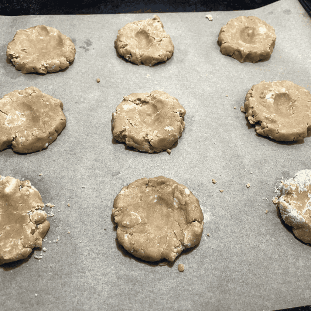 rolled chilled cookie dough balls with divit in the middle on parchment on baking sheet