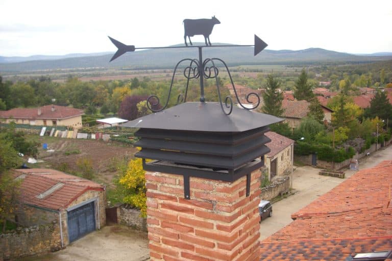 Reja de protección con chimenea y veleta de gallo en el techo de una casa rural, servicios de cerrajería Osfran en acción.