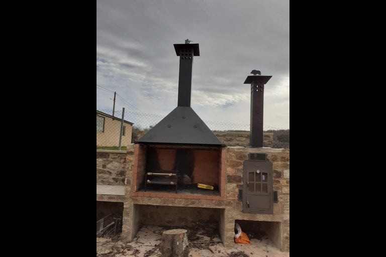 Chimenea de piedra con estructura metálica y accesorios para barbacoa en espacio exterior al aire libre.