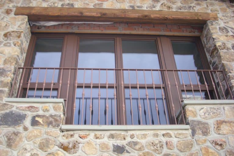 Rejas robustas de hierro para ventanas en construcción de piedra, seguridad y estética en vivienda rural.