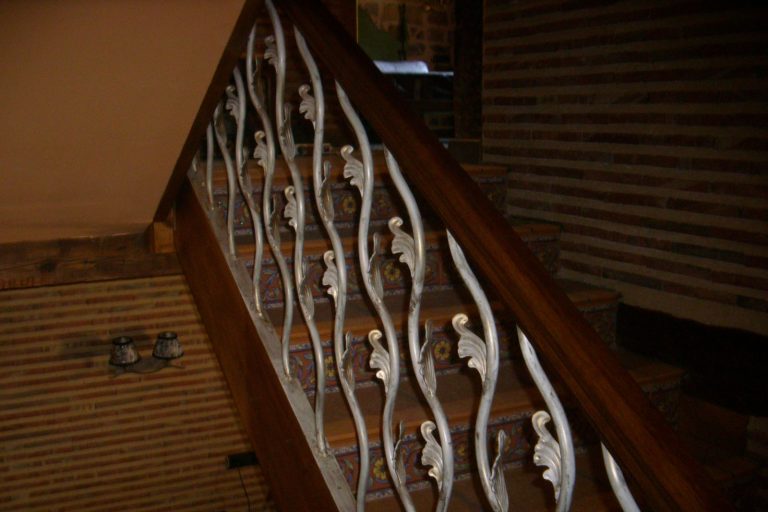 Puerta de escalera con barandilla de hierro y madera, estilo clásico y decorativo en interior.