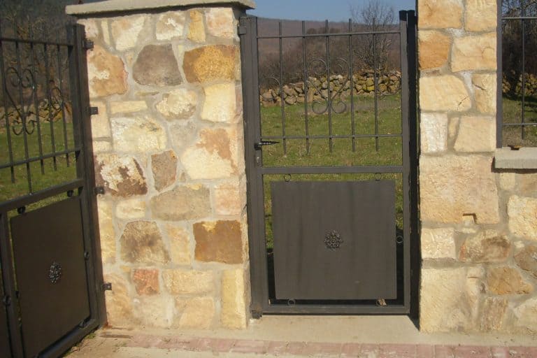 Puerta de jardín de hierro con estructura de piedra y decorativos en el diseño. Celosía para entrada segura y elegante.
