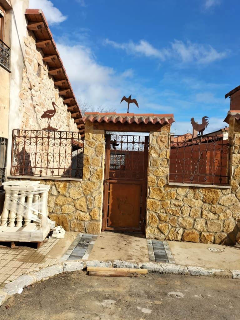 Puerta de herrería decorada con motivos animales, en fachada de piedra rústica, ideal para seguridad y estética.