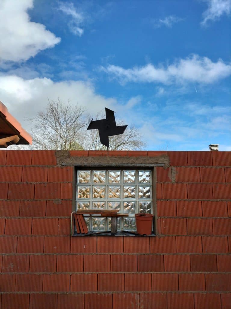 Puerta de obra con ventana de bloques de vidrio, caja de madera y maceta, cielo azul con nubes.