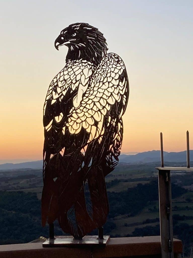 Escultura de águila en hierro en paisaje natural al atardecer.