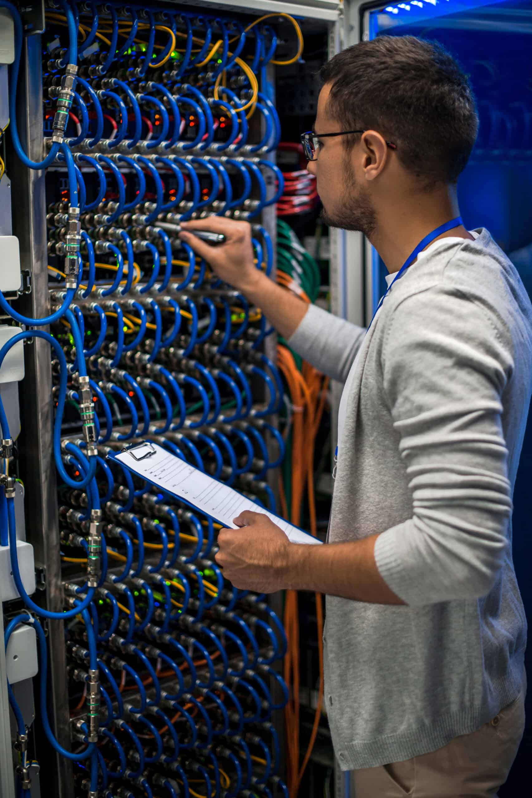 A person holding a clipboard inspects and adjusts cables in a server room filled with blue network wires and equipment, ensuring optimal performance for WordPress hosting.