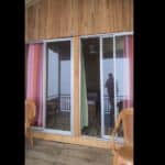 Sliding glass doors leading to a cozy wooden balcony with pink and green curtains in a charming retreat.