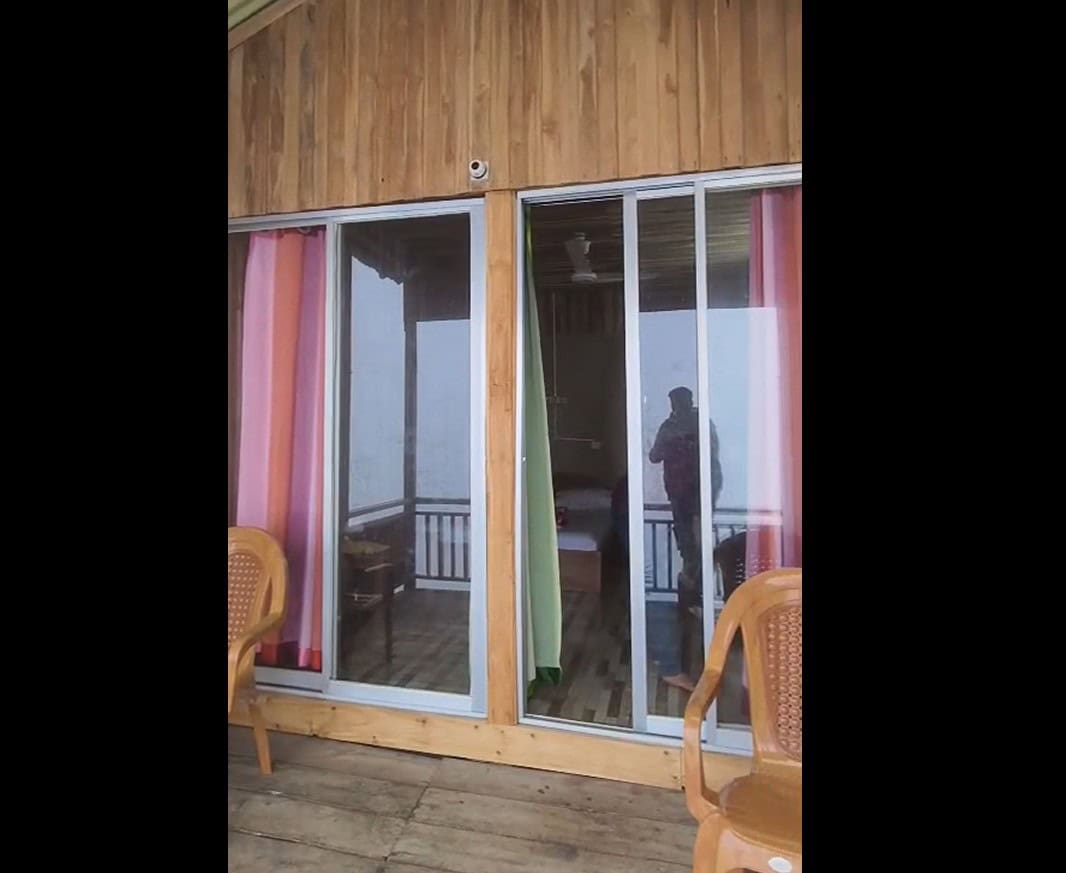 Sliding glass doors leading to a cozy wooden balcony with pink and green curtains in a charming retreat.
