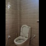 Toilet with bidet spray in a bathroom with beige tiled walls, emphasizing clean and functional design.