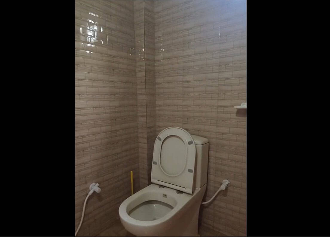 Toilet with bidet spray in a bathroom with beige tiled walls, emphasizing clean and functional design.