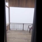 Vivid mountain view from cozy wooden balcony with chair during foggy weather, perfect for relaxation and enjoying nature.