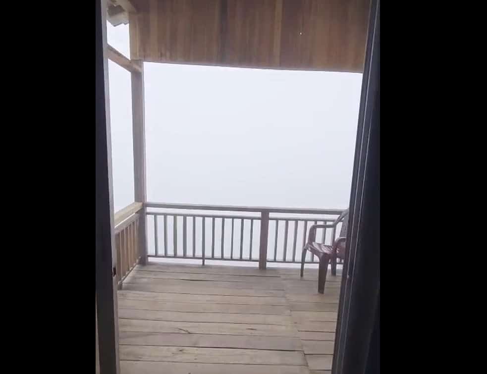 Vivid mountain view from cozy wooden balcony with chair during foggy weather, perfect for relaxation and enjoying nature.