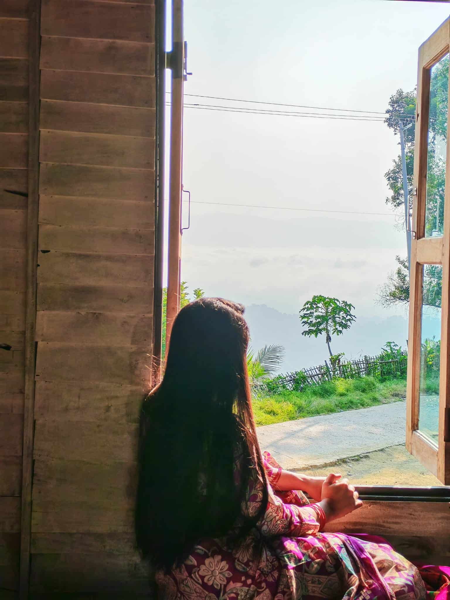 Serene woman enjoying peaceful mountain view from wooden cabin window, symbolize mindfulness and connection with nature.