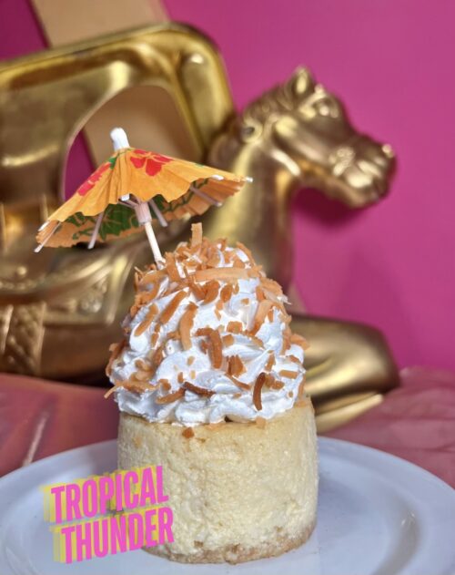 Delicious mini Pina Colada cheesecake topped with whipped cream, toasted coconut, and a decorative u.