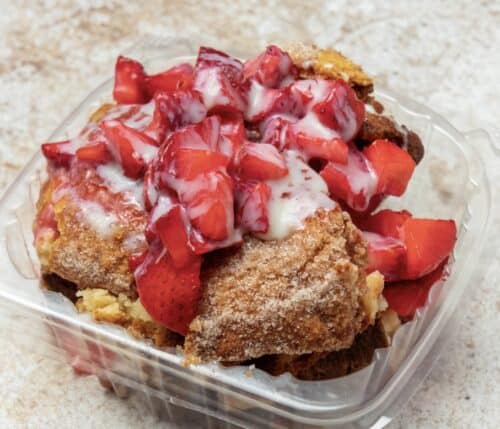 Churro cheesecake topped with fresh strawberries and strawberry sauce.