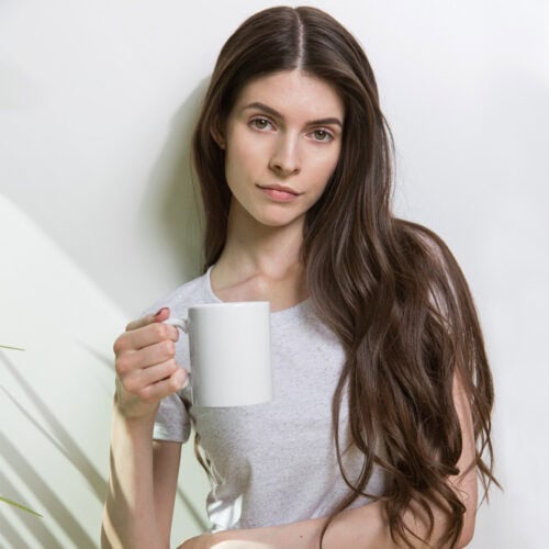 White glossy ceramic mug held by a woman with long brown hair.