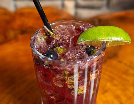 Refreshing berry lime cocktail with fresh berries and lime wedge in a tall glass.