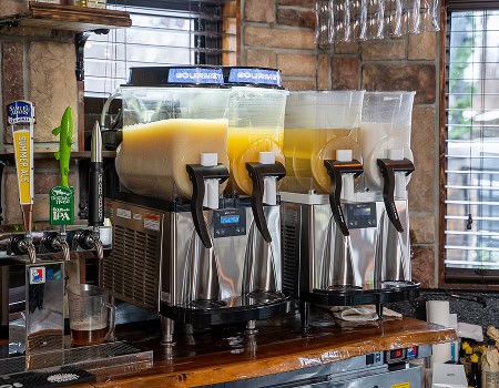 Juice dispensers with orange, pineapple, and other fruit juices on a wooden bar.