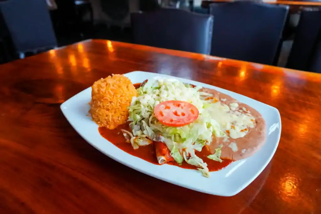 Authentic Mexican dish with rice, lettuce, tomato, and a crispy side item on a white plate.