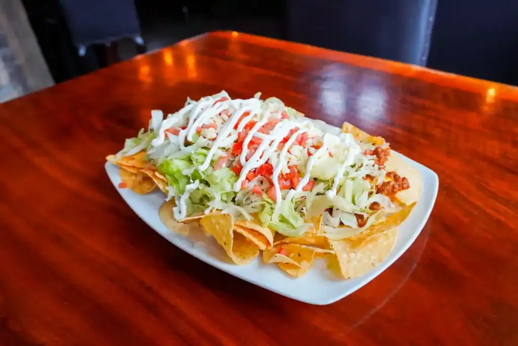 Delicious Mexican nachos with cheese, lettuce, and salsa on a white plate.