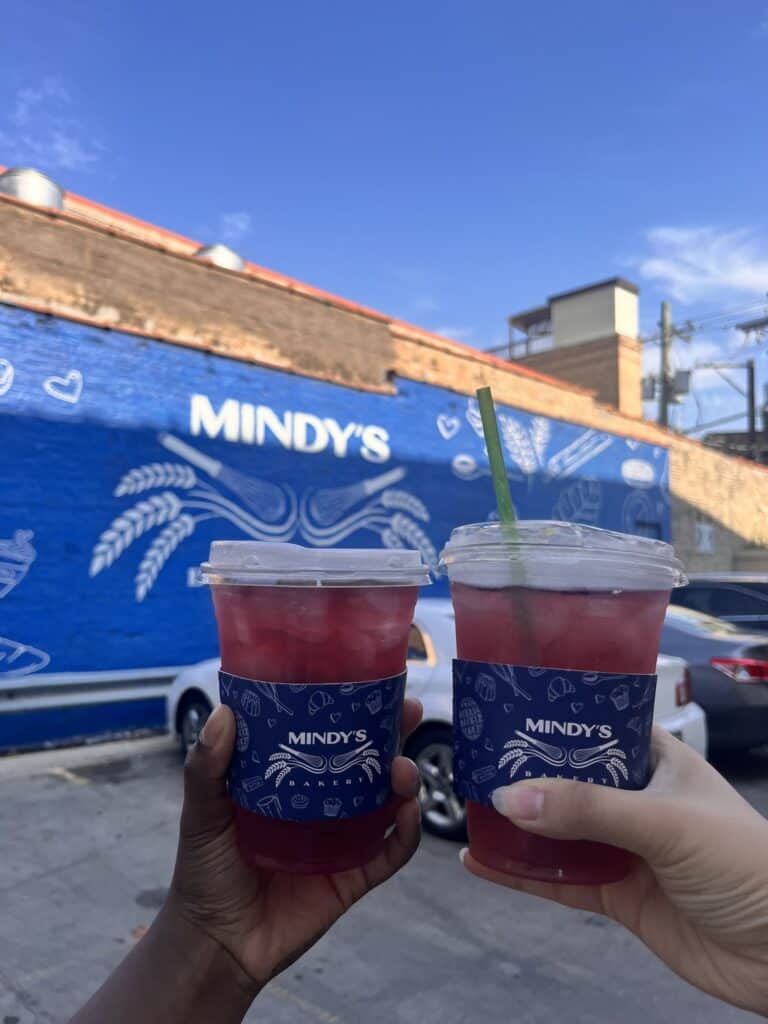 Two iced tea drinks in front of Mindy's Bakery wall