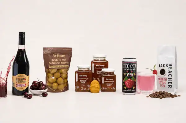 A lineup of gourmet food items including wine, cherries, olives, jars of honey, a can drink, a coffee bag, and scattered coffee beans, all displayed on a white background.