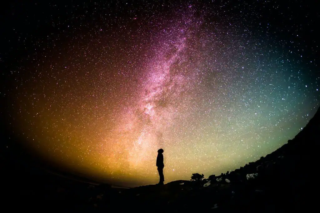 Vast starry night sky with Milky Way galaxy and colorful cosmic clouds, person silhouette gazing at the universe, representing exploration and financial growth with Chrysalis BTC.