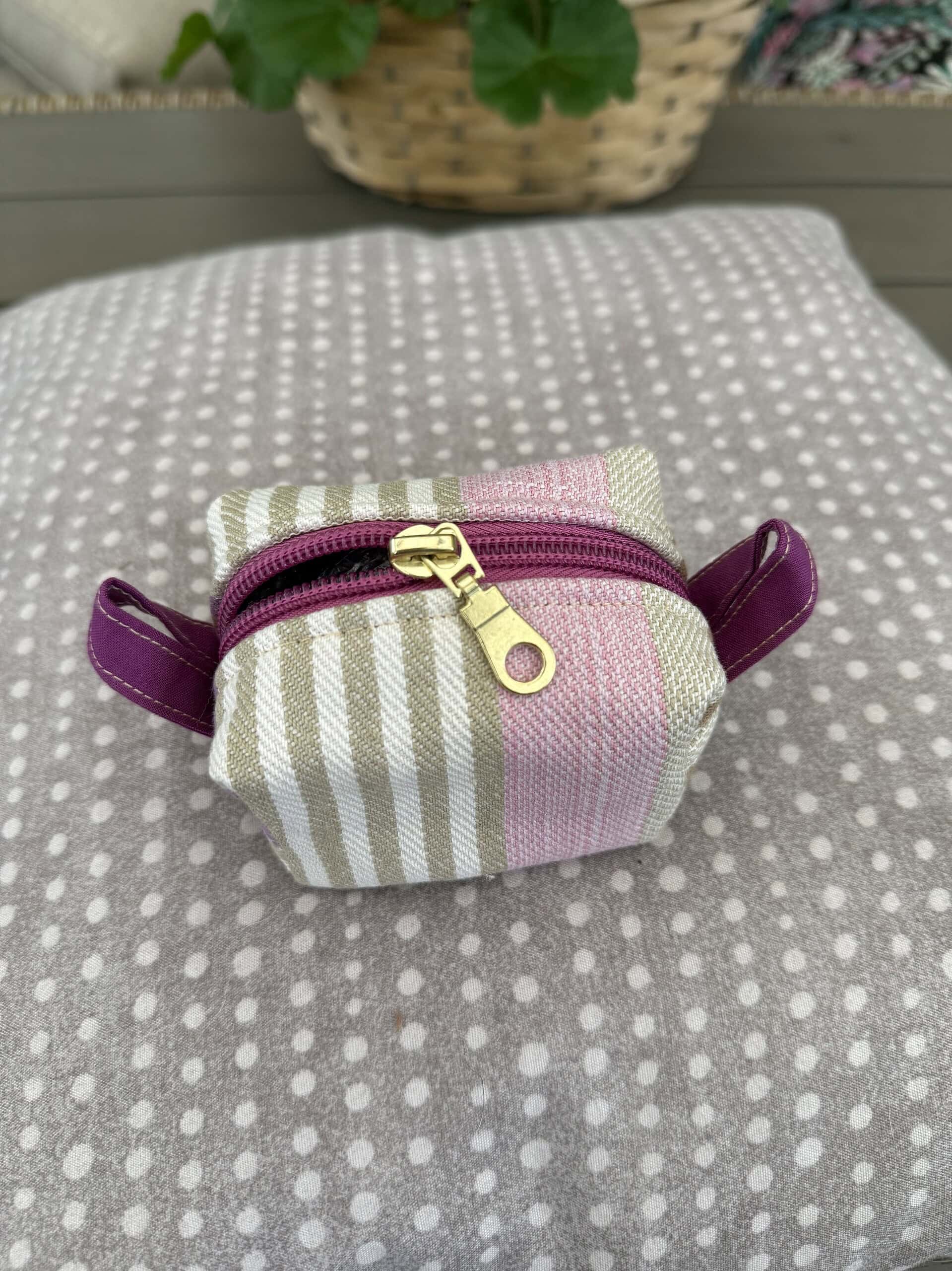 Liten tygpåse med rosa och beige ränder och guldfärgad dragkedja, placerad på en grå polkadottyg. En liten förvaringslösning för småsaker, perfekt för organisering och förvaring.