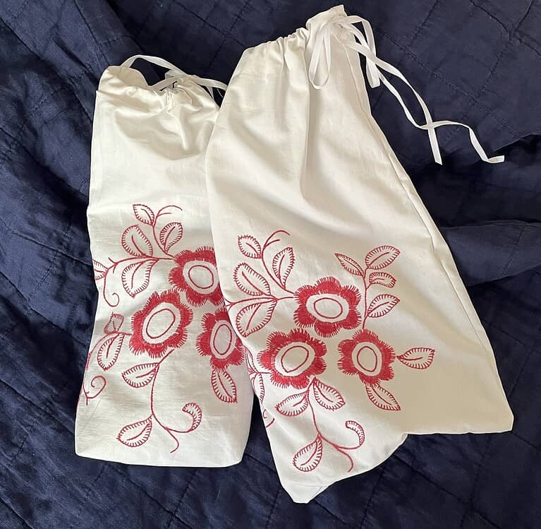 Sv_SE/alt text: Two white tygpåsar med röda blomster- och bladmönster från CircleSign, perfekta för miljövänlig shopping eller som presenter.